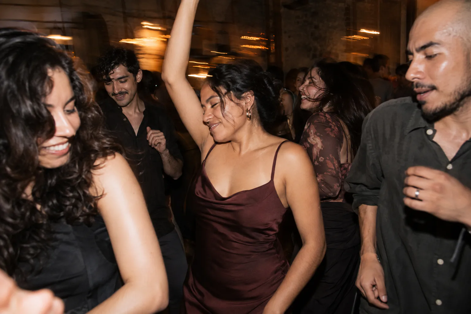 Amigos bailan y ríen en una pista de noche, entre luces en movimiento.